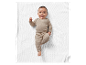 Bébé souriant vêtu de vêtements beiges sur une couverture blanche.