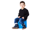 Garçon en pull noir, jean et bottes bleues assis sur un pouf bleu.