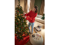 Femme décore un sapin de Noël avec des boules et des cadeaux dans le salon.