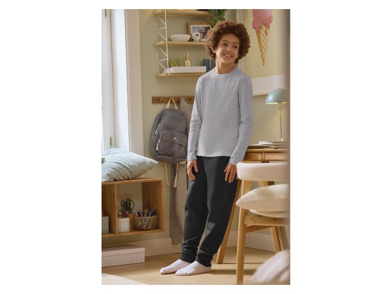 Garçon en t-shirt gris à manches longues et pantalon de survêtement noir dans une chambre.