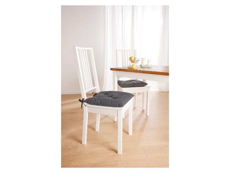 Deux chaises blanches avec des coussins gris dans une salle à manger