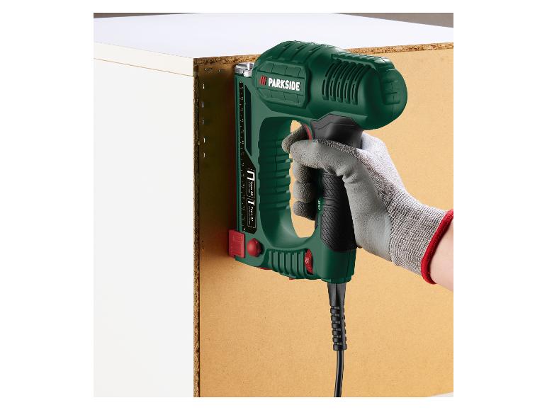 Main tenant une agrafeuse électrique, fixant un panneau de bois à une armoire blanche.