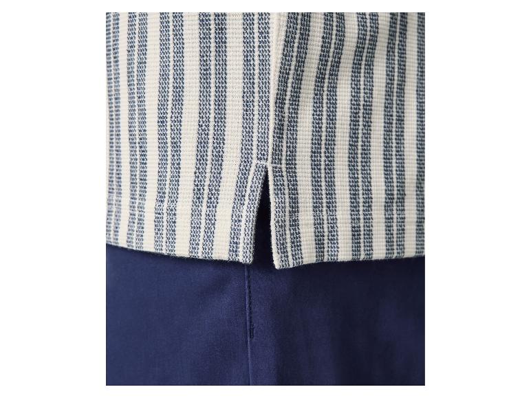 Gros plan d'un haut rayé bleu et blanc avec une fente latérale, associé à un pantalon bleu marine.