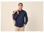 Homme en chemise boutonnée bleu marine et pantalon beige, veste beige sur l'épaule.