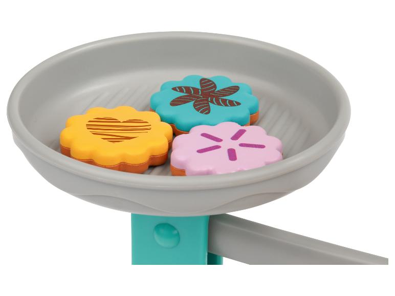Trois biscuits jouets colorés dans une poêle grise.