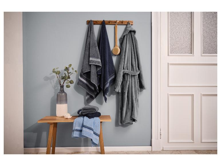 Salle de bain avec serviettes, peignoir et banc en bois avec vase et coquillage.
