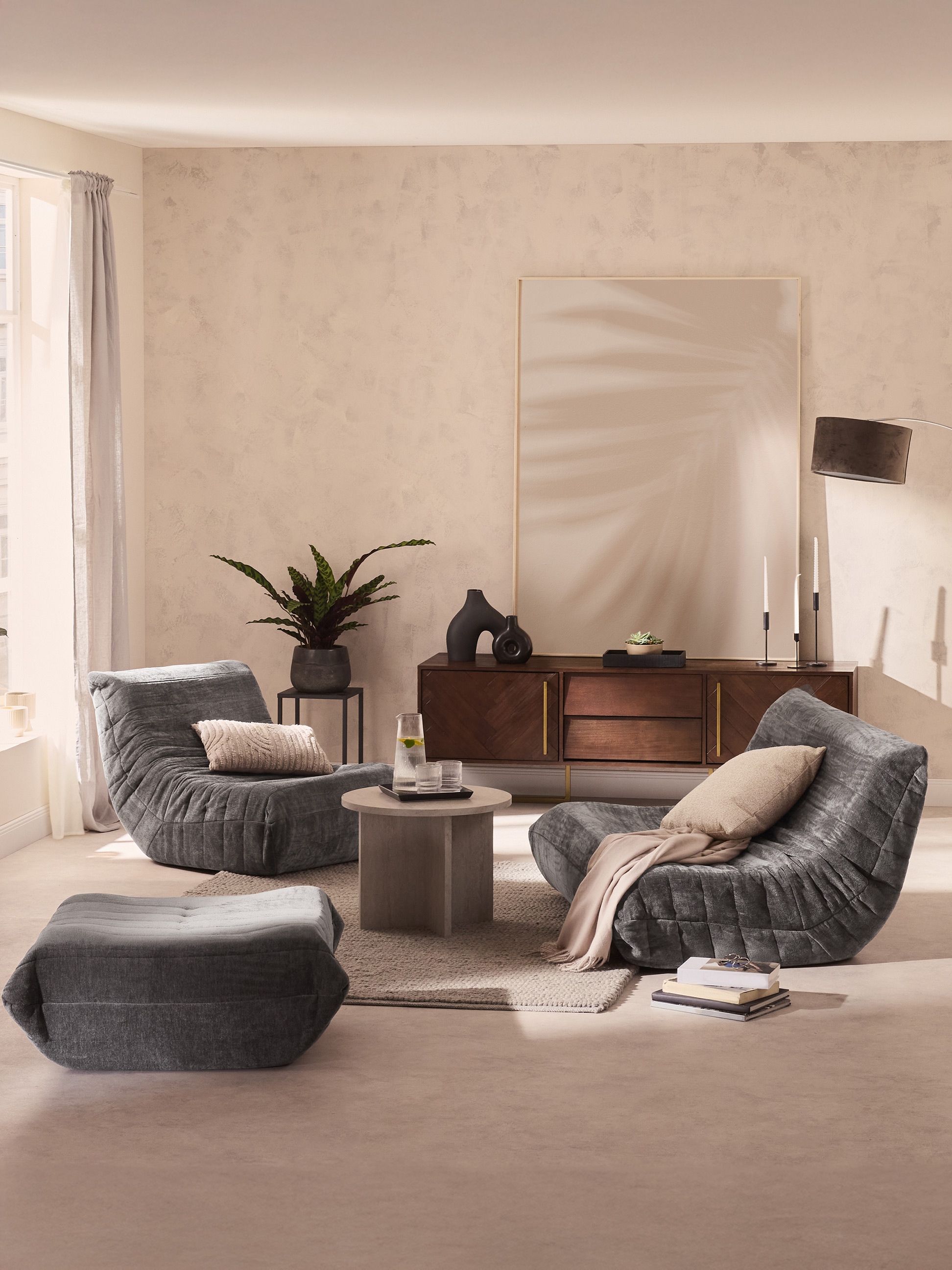 Salon moderne avec fauteuils gris confortables, table basse et buffet en bois.