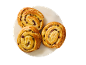 Trois pains aux raisins dorés sur une assiette blanche sur fond noir.