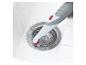 Une brosse avec un bouton rouge nettoie un évier.