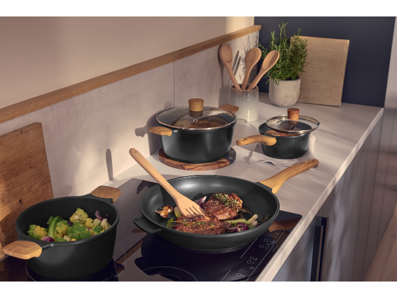 Casseroles et poêles noires avec poignées en bois sur une plaque à induction dans la cuisine.