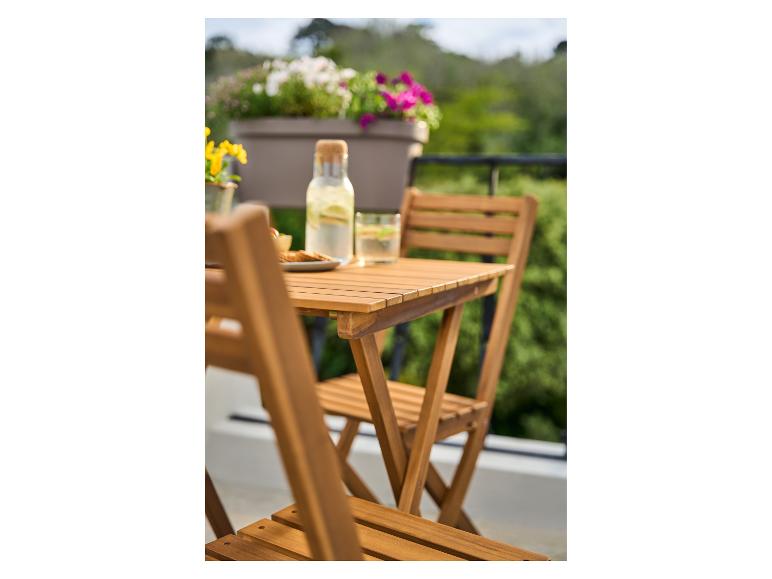 Bouteille d'eau en verre et collations sur une table de balcon en bois, avec des fleurs et de la verdure en arrière-plan.