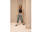 Une femme vêtue d'un gilet noir et d'un pantalon à motifs fait un pas en avant.