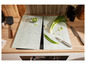 Deux planches à découper en verre avec des oignons verts, un couteau et une spatule sur un comptoir en bois.