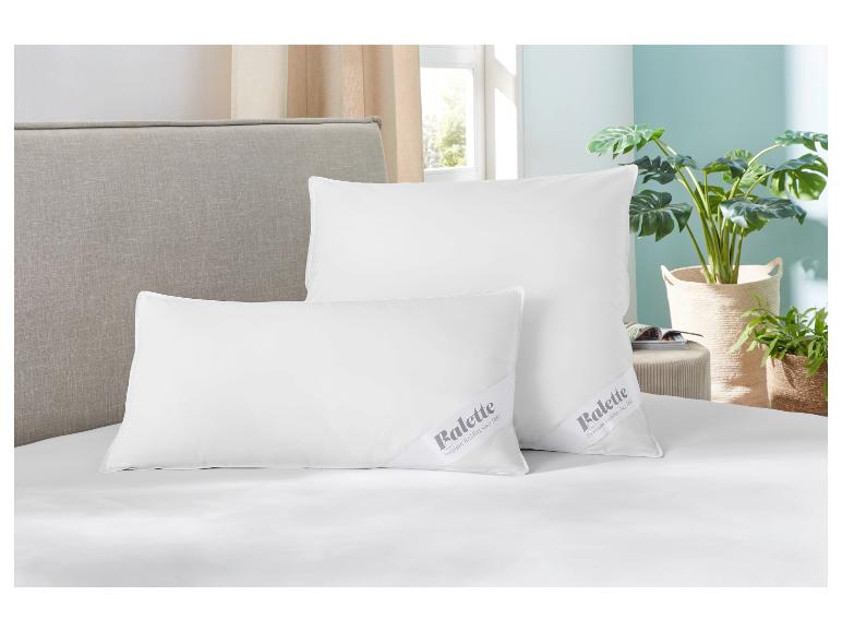 Deux oreillers Balette blancs sur un lit avec une tête de lit gris clair et des plantes