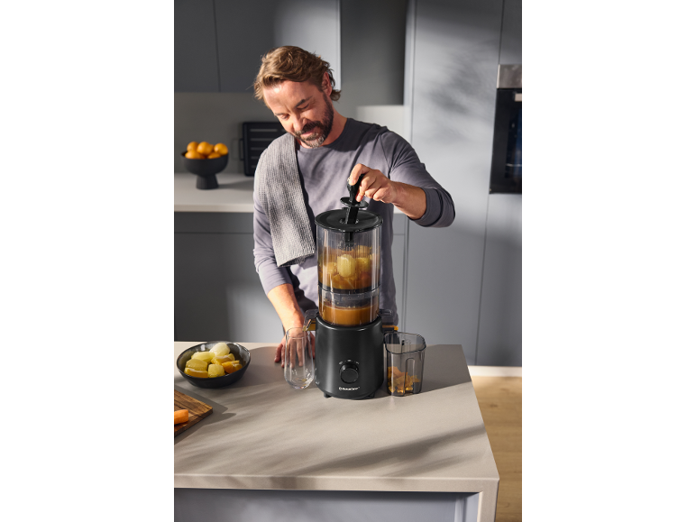 Homme utilisant un extracteur de jus pour faire du jus frais dans une cuisine moderne.