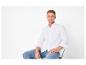 Homme en chemise blanche et jean assis sur une chaise.