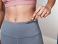 Une femme portant un legging gris et un soutien-gorge de sport rose avec une clé dans sa poche.