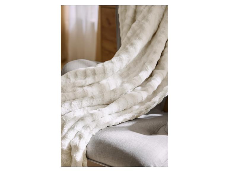 Plaid doux et douillet en fausse fourrure crème sur un fauteuil gris.