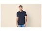 Homme en polo bleu marine avec détails rayés bleus et jean.