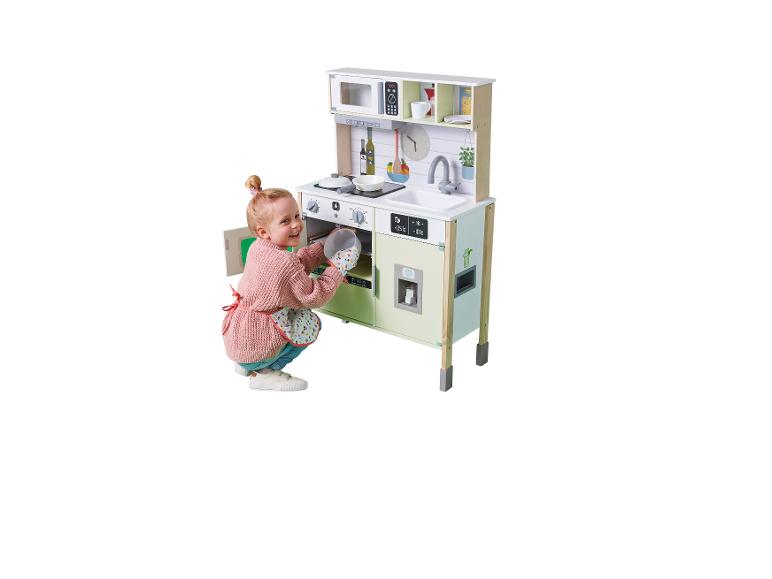 Petite fille souriante en tablier met un plat dans le four d'une cuisine de jeu en bois.