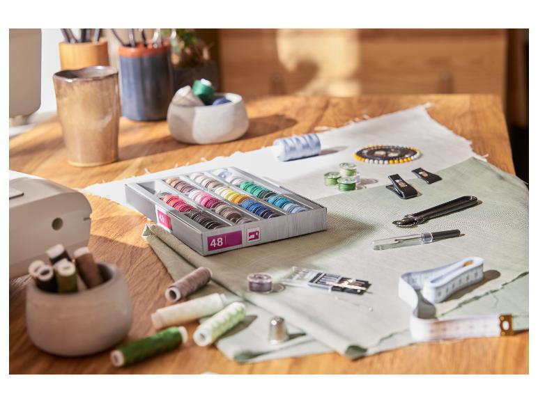 Un kit de couture avec 48 bobines de fil de diverses couleurs, des outils de couture et du tissu sur une table en bois.