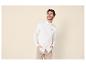 Homme en chemise blanche et pantalon beige, souriant les mains dans les poches.