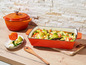 Un plat à gratin en fonte orange avec un plat végétarien de courgettes, tomates, brocolis et feta.
