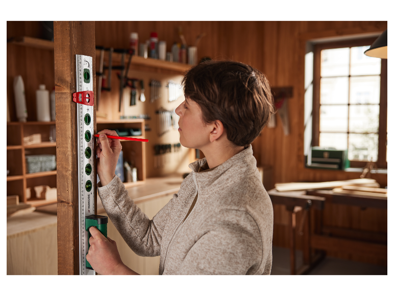 Une femme utilise un niveau Parkside et un crayon dans un atelier pour marquer du bois.