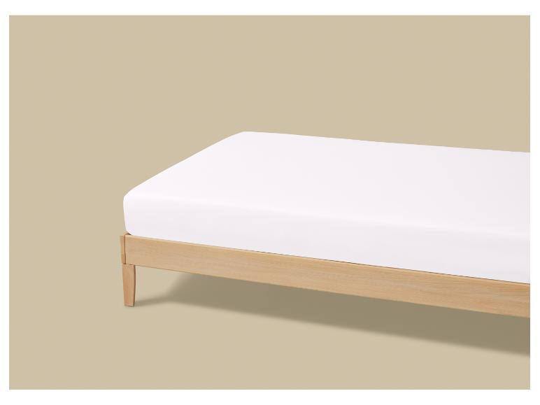 Lit en bois avec matelas blanc sur fond beige.