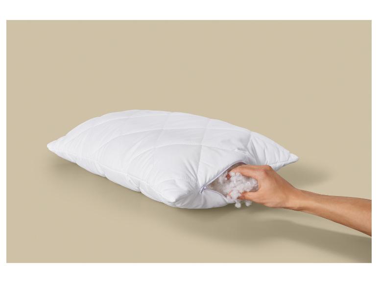 Oreiller blanc matelassé avec fermeture éclair, rempli de matière moelleuse, tenu par une main.