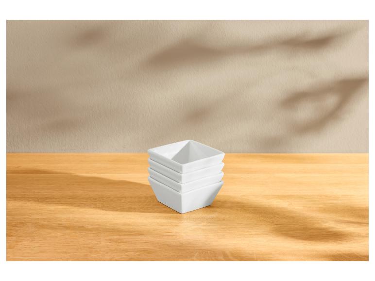 Pile de bols carrés blancs sur une table en bois avec des ombres de feuilles.
