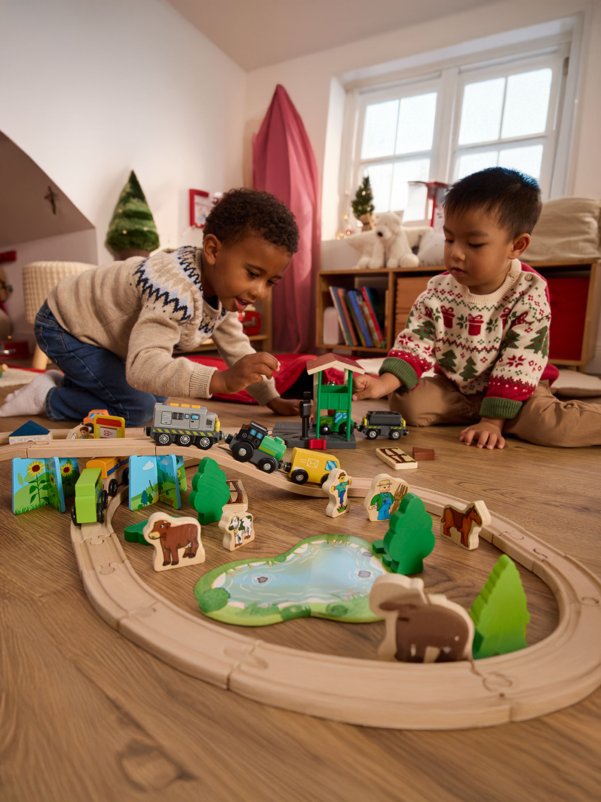 Deux garçons jouent avec un train en bois et des figurines d'animaux de la ferme sur le sol.