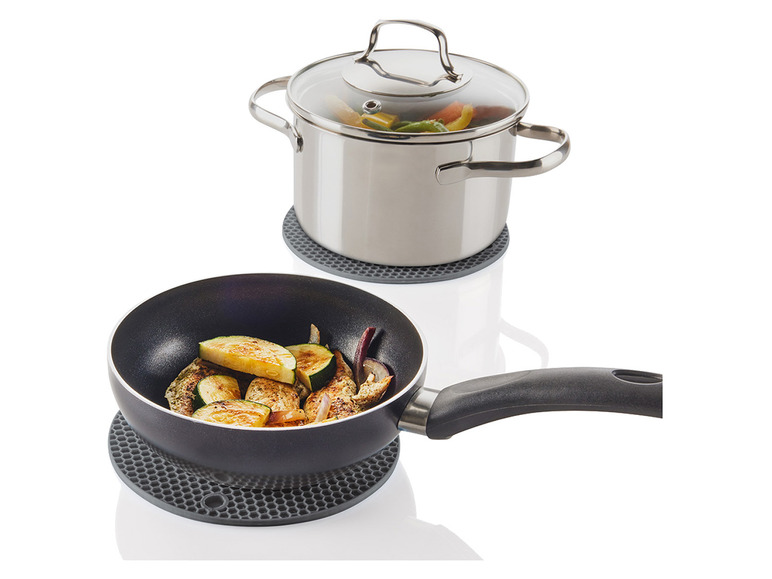 Une casserole et une poêle avec couvercle sur des dessous de plat en silicone résistant à la chaleur.