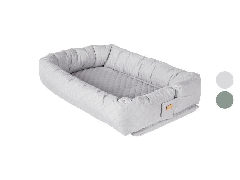 Nid de bébé matelassé gris clair avec une petite étiquette en bois, présenté avec des échantillons de couleurs.
