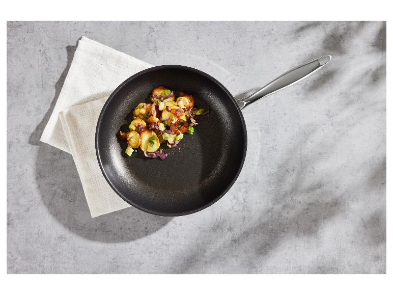 Poêle avec pommes de terre rôties et légumes sur une surface grise.