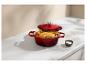 Cocotte en fonte rouge avec poulet rôti et légumes sur un comptoir blanc.
