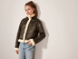 Une femme porte une veste en cuir marron avec une doublure blanche et un jean bleu.