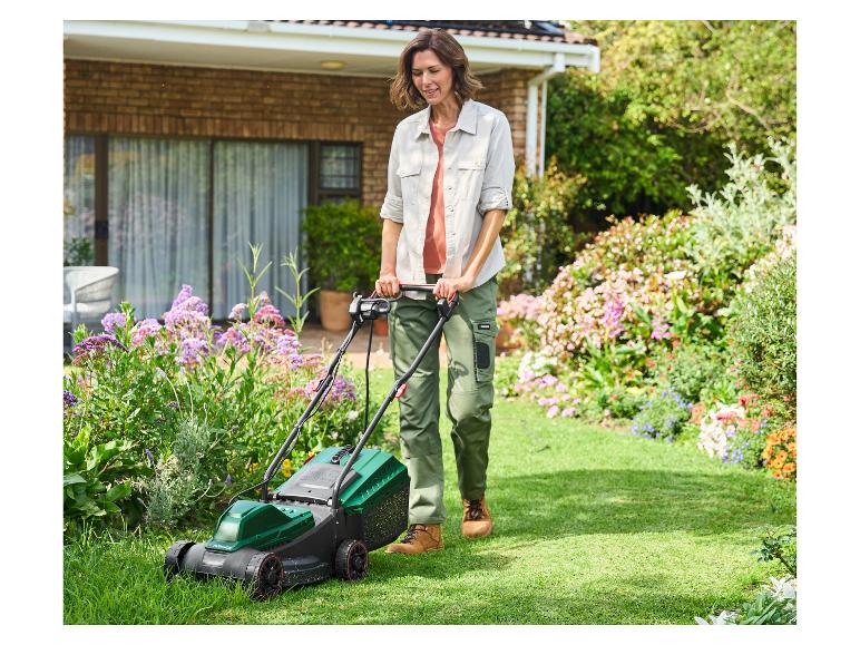 Femme tondant la pelouse avec une tondeuse Parkside dans le jardin d'une maison.