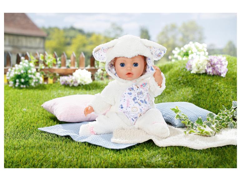 Poupée BABY born en costume d'agneau sur une couverture dans l'herbe avec des coussins et des fleurs.