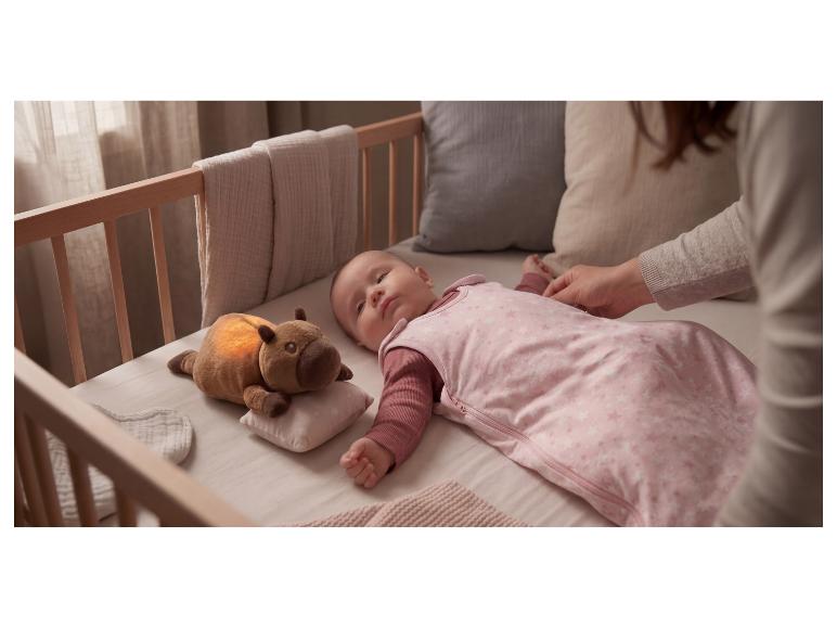 Bébé dans une gigoteuse rose dans un berceau, avec une peluche lumineuse à côté.