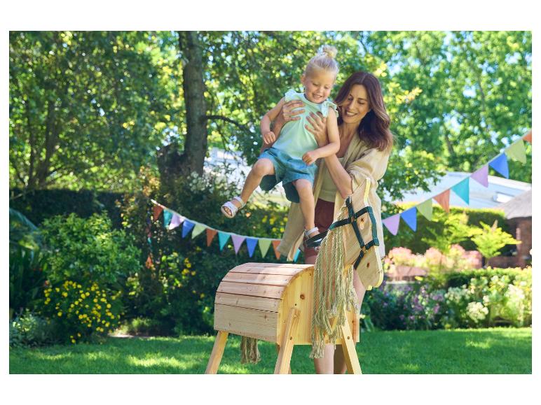 Mère et enfant jouant avec un cheval à bascule en bois dans le jardin.