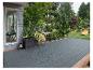 Revêtement de terrasse gris avec bords en bois, entouré de verdure luxuriante et d'un jardin.