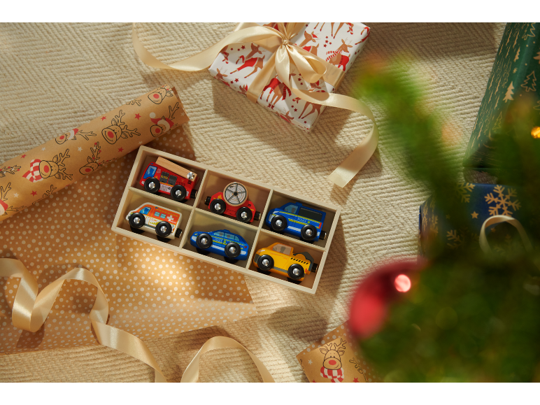 Voitures jouets en bois dans une boîte, cadeaux emballés et sapin de Noël.