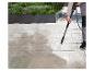 Personne nettoyant une terrasse avec un nettoyeur haute pression, enlevant la saleté des carreaux clairs.