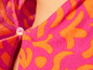 Gros plan sur un vêtement rose et orange à fleurs avec un bouton.
