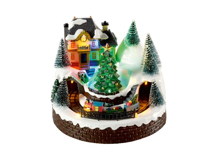 Scène de Noël illuminée avec un train, une gare et des arbres enneigés.