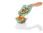 Une main verse des légumes coupés d'une planche à découper verte dans un bol en verre avec de la salade.