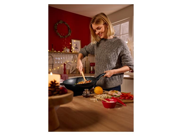 Femme souriante préparant un sauté dans un wok, avec des ingrédients frais sur le comptoir.