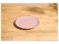 Assiette rose sur une table en bois clair avec lumière du soleil et ombres.