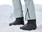 Bottes de neige noires avec un pantalon de ski gris sur la neige.
